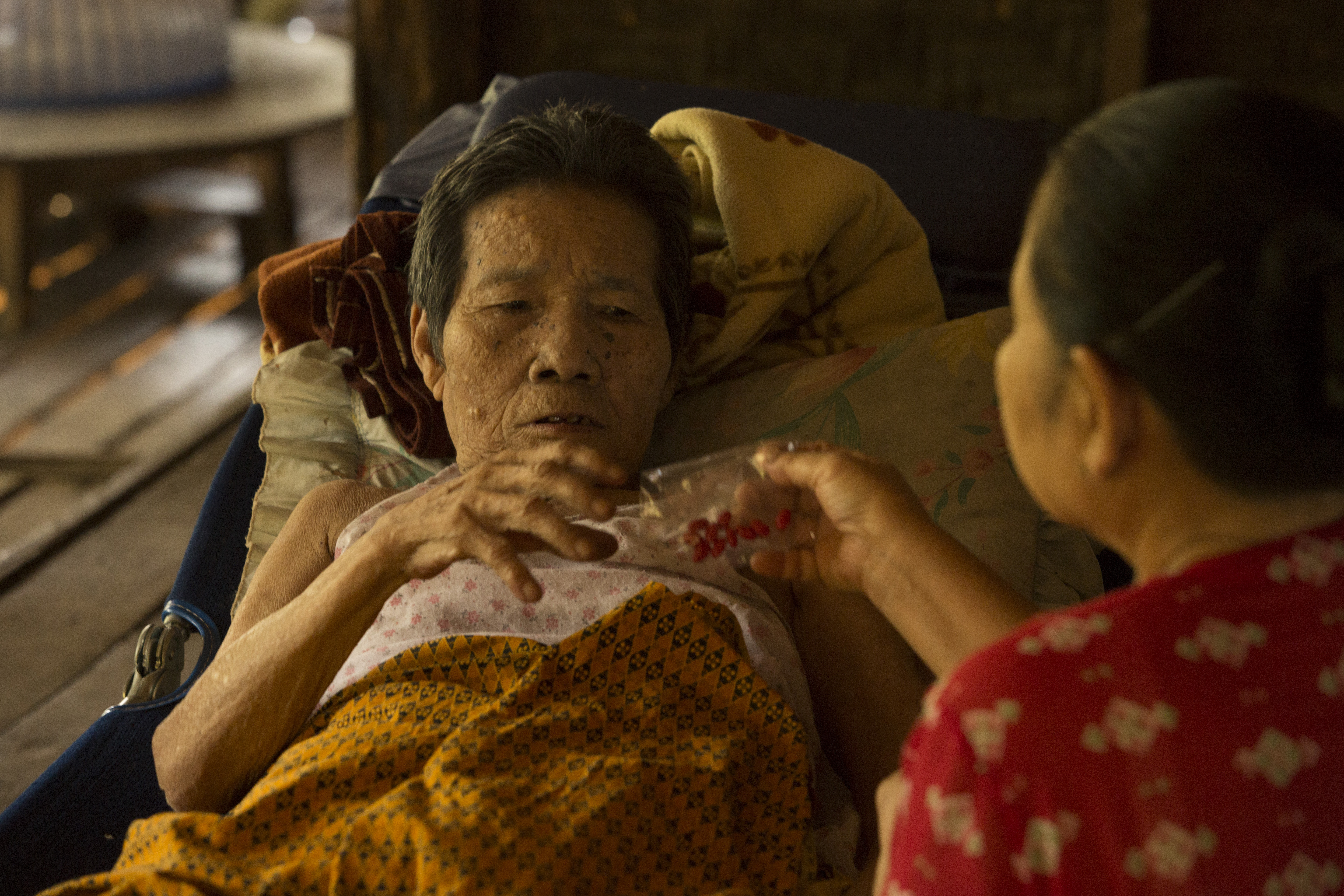 An older woman in Myanmar is given medication by a home care volunteer.