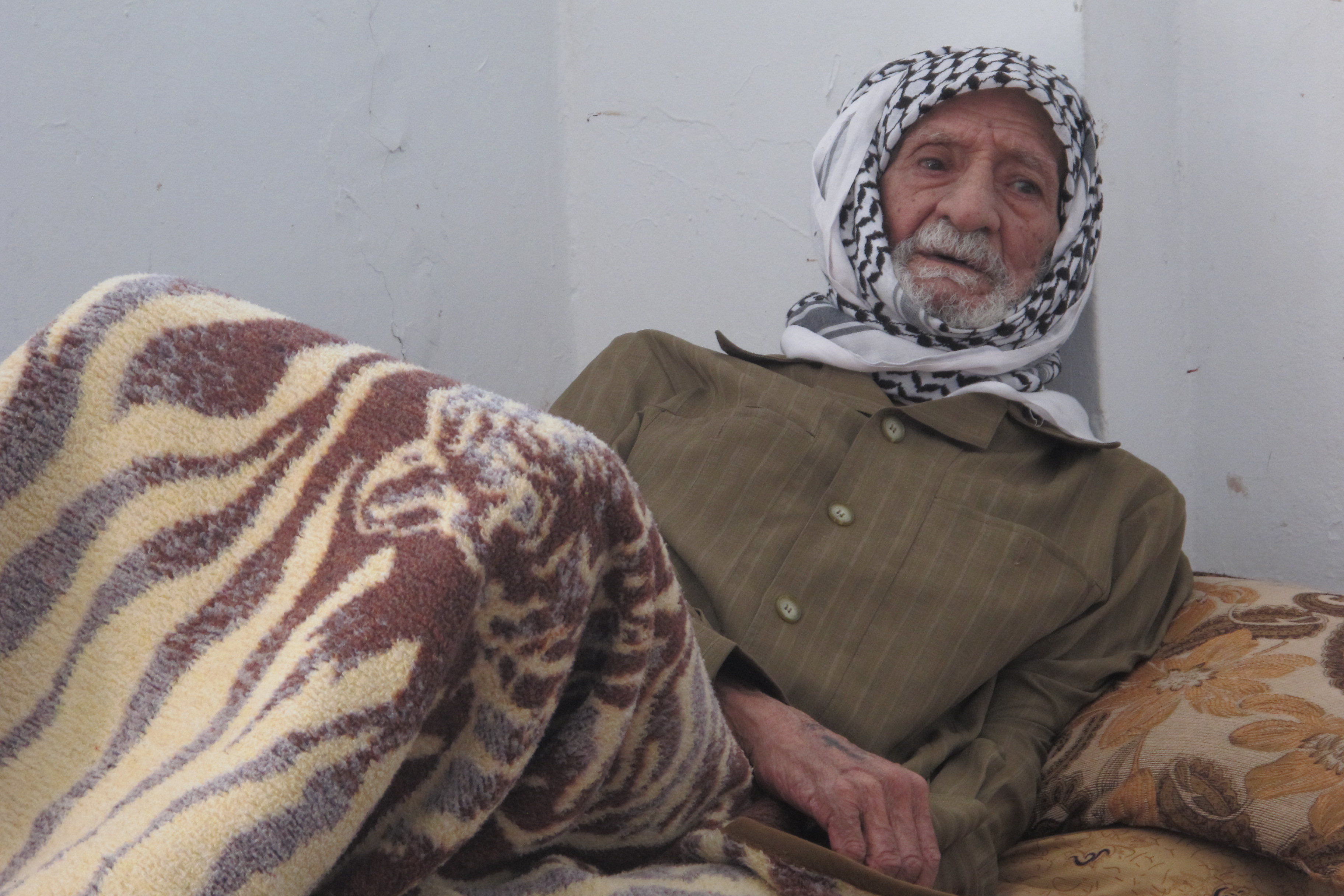 An older Syrian refugee sits up in bed in Jordan.