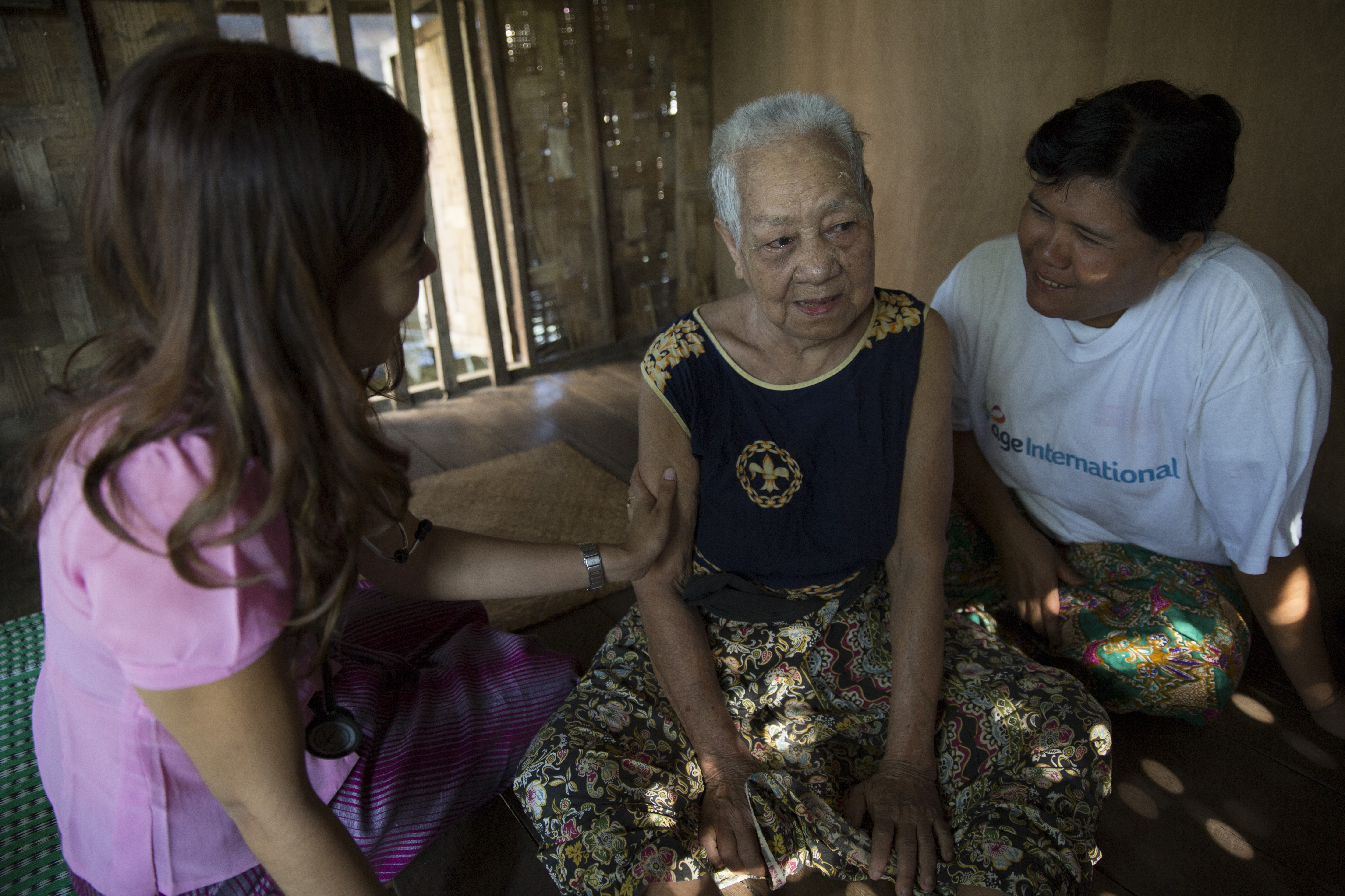 A carer and a doctor sit around an older woman with dementia in Myanmar.