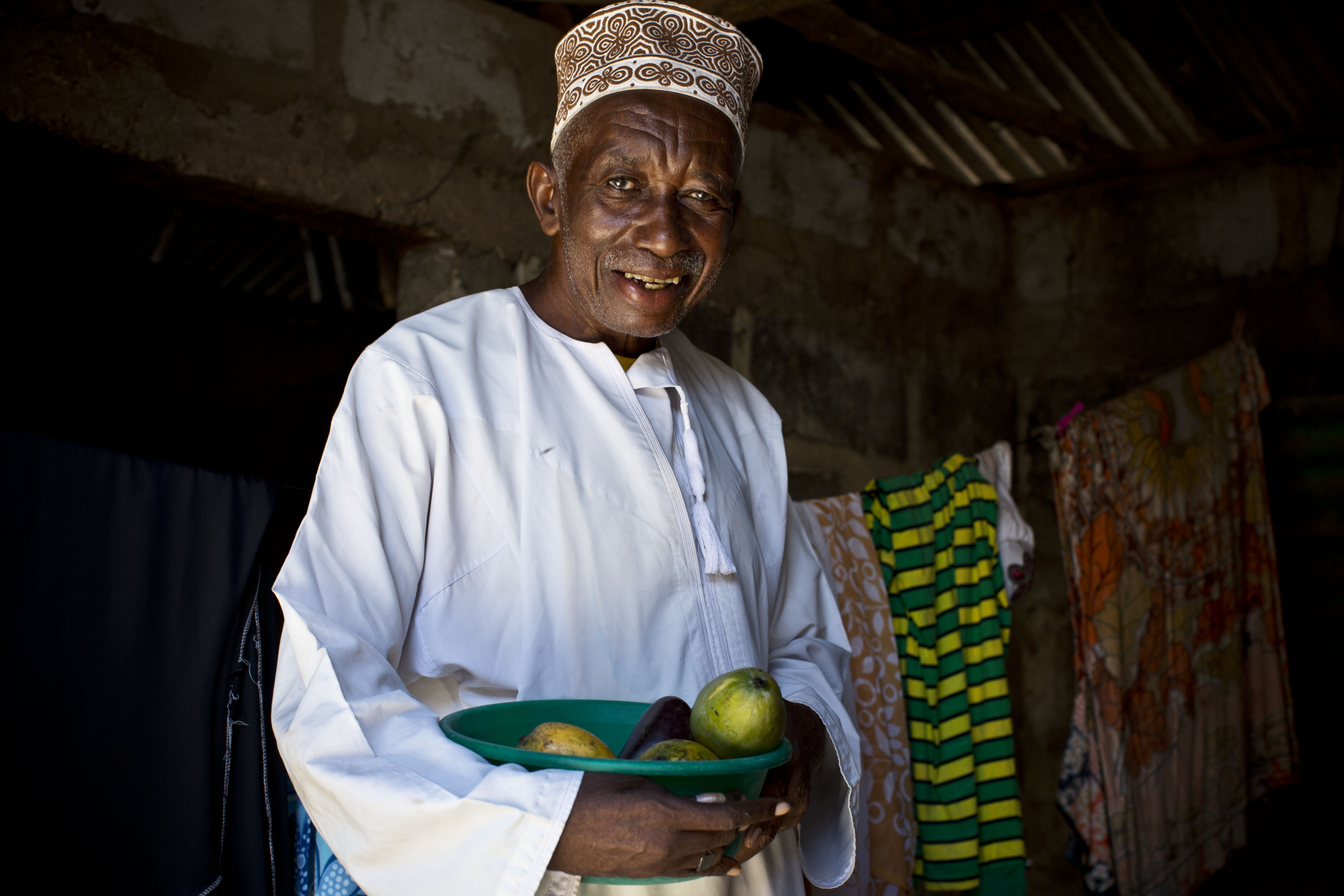 Older man in Zanzibar stands holding a bowl of fruit.